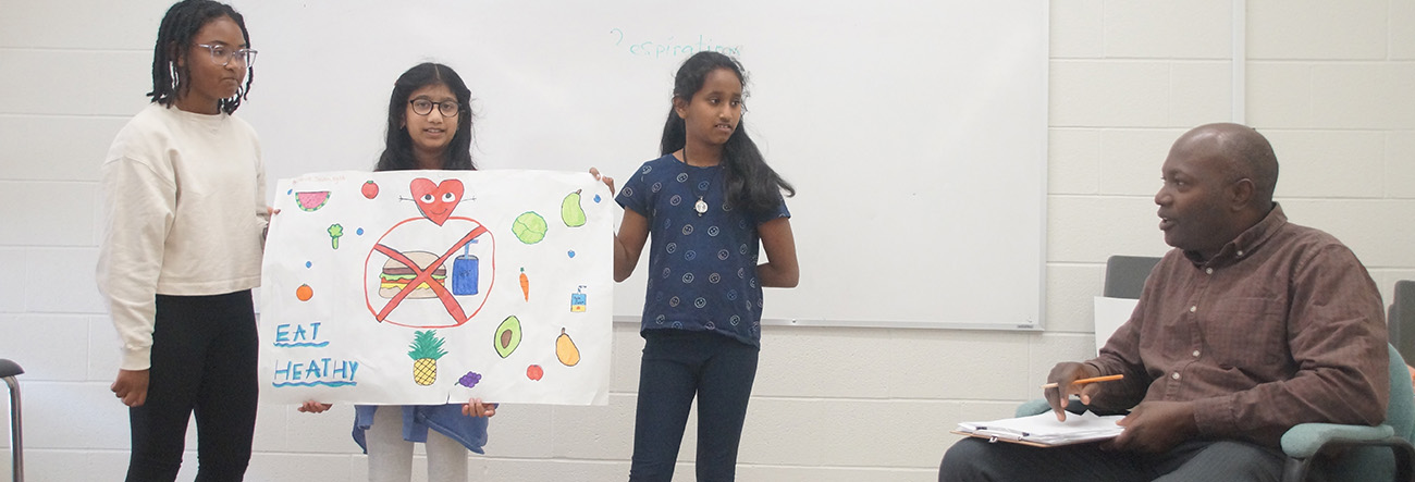 Three female students presenting a project in front of a male educator
